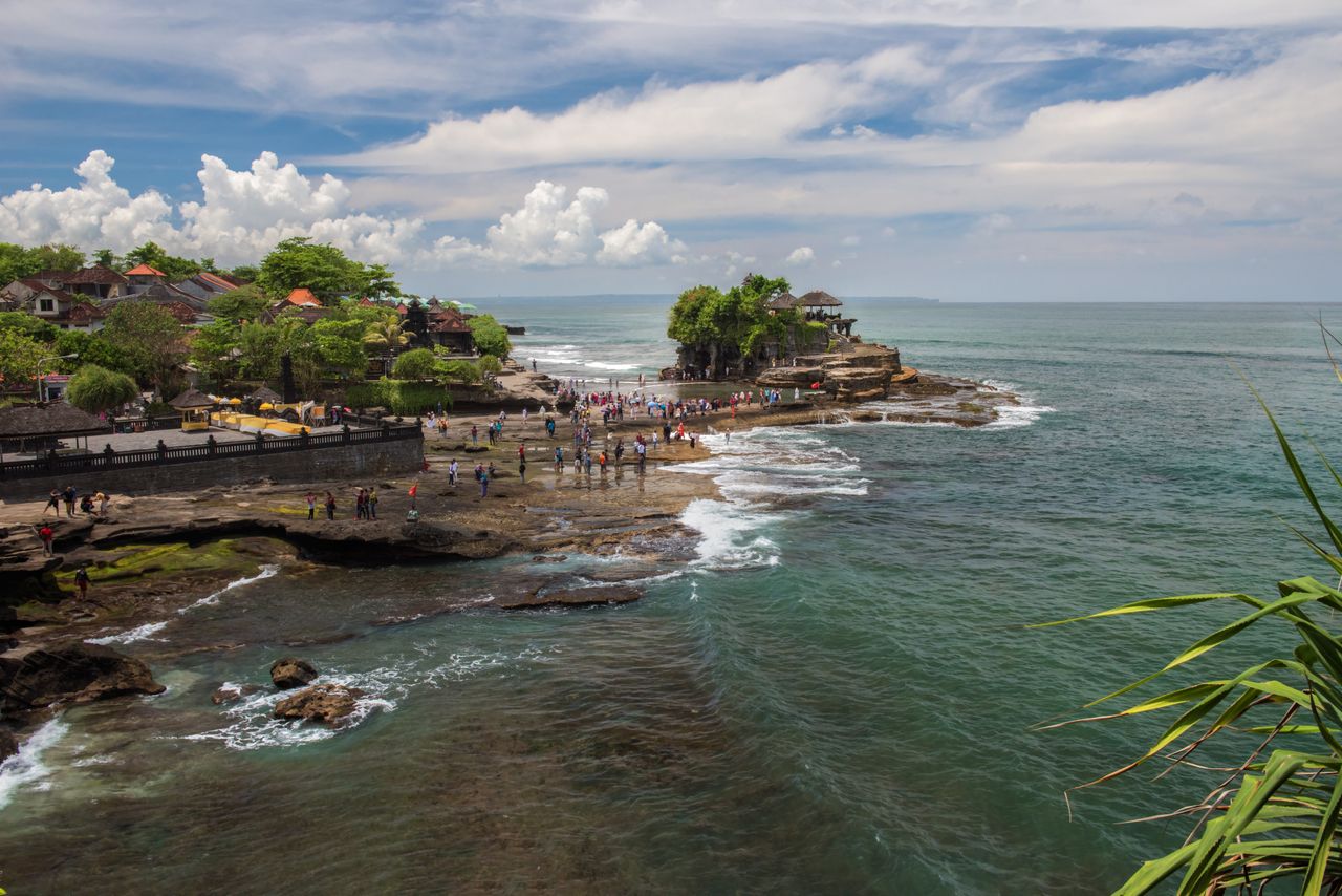 Home A breathtaking view of Tanah Lot Temple surrounded by the ocean in Bali, Indonesia with tourists exploring the area.