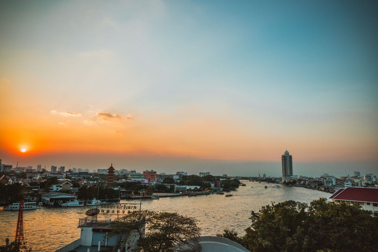 Home Stunning sunset view over Bangkok's Chao Phraya River with cityscape and skyline.